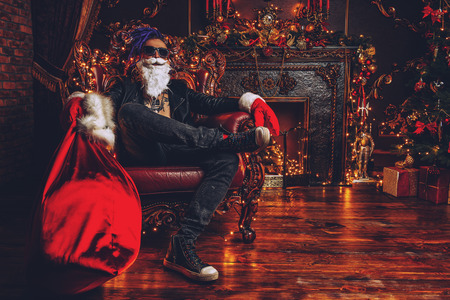 Ð¡heerful punk Santa with a bag of gifts in his hands  in luxurious apartments decorated for Christmas. Bad Santa concept.の写真素材