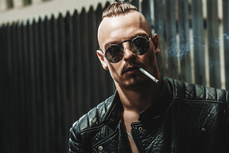 Close-up portrait of a punk man smoking a cigarette on the street. Fashion, subculture.の写真素材