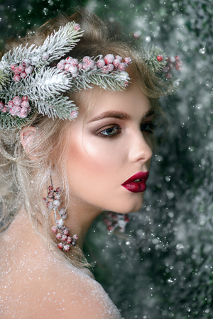 Close-up portrait of a beautiful young woman with christmas tree in hairstyle and holiday make-up over snow-covered green background. Beauty, fashion.の写真素材