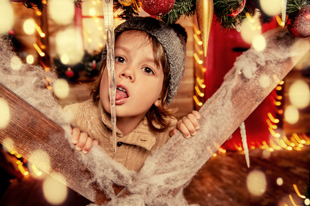 A little boy sitting on the porch of the house decorated for Christmas. Miracle time. Merry Christmas and Happy New Year.の写真素材