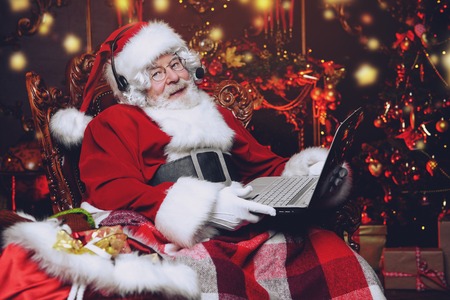A portrait of Santa Claus sitting at his home with a laptop. Miracle time. Christmas, New Year.の写真素材
