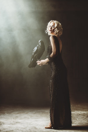 A full length portrait of a beautiful blonde lady with a raven. Evening dress. Fashion, beauty.