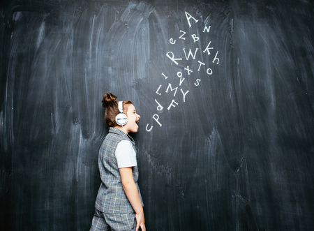 A portrait of a cute girl with headphones standing over a blackboard. School, education.の写真素材