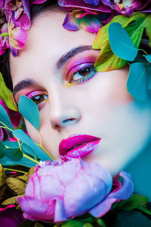 Beauty portrait. Beautiful brunette woman with sensual lilac lips surrounded by flowers. Spring look. Cosmetics, make-up. Perfumery.の写真素材
