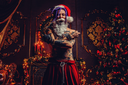 Bad Santa concept. Portrait of a nude tattooed Santa with purple dreads demonstrating antisocial behavior, rudeness and aggression.の写真素材