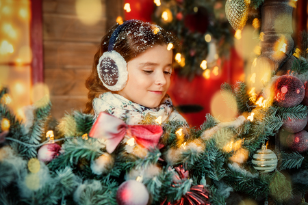 A cute girl is on the porch of the house decorated for Christmas. Merry Christmas, Happy New Year. Miracle time.の写真素材