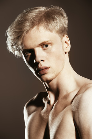 Portrait of a shirtless young man with blond hair posing at studio. Gray background. Men's health.の写真素材