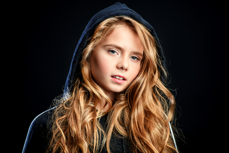 A close-up portrait of a cute emotional girl posing over the black background in studio. Beauty, fashion for kids and teenagers.の写真素材