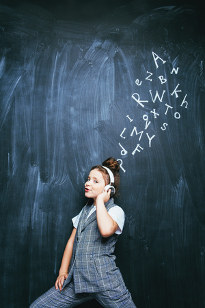 A portrait of a cute girl with headphones standing over a blackboard. School, education.の写真素材