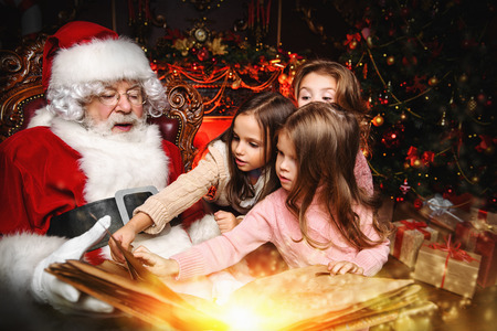 Happy young girls are sitting with Santa Claus at home. Merry Christmas and Happy New Year. Miracle time.の写真素材
