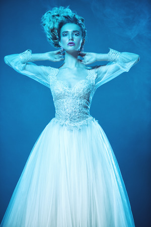 A portrait of a cold beautiful lady wearing a fluffy dress and posing in the studio over the blue background. Beauty,cosmetics, hairstyle, fashion.の写真素材