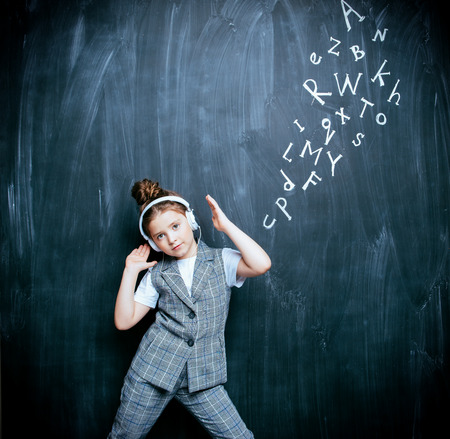 A portrait of a cute girl with headphones standing over a blackboard. School, education.の写真素材