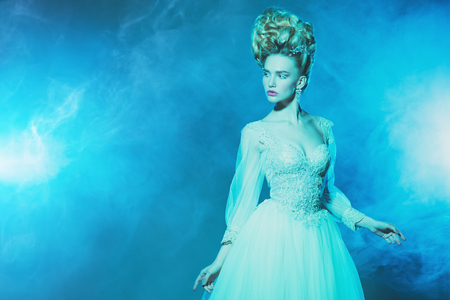 A portrait of a cold beautiful lady wearing a fluffy dress and posing in the studio over the blue background. Beauty,cosmetics, hairstyle, fashion.の写真素材