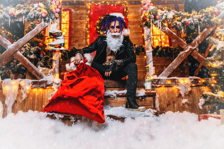 Cool punk Santa is sitting around near his house with a bag of gifts in his hands.の写真素材