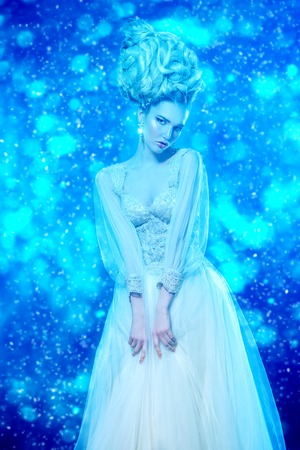 A portrait of a cold beautiful lady wearing a fluffy dress and posing in the studio over the blue background. Beauty,cosmetics, hairstyle, fashion.の写真素材