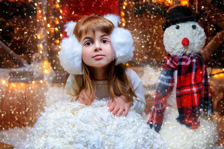 Cute child girl sculpts a snowman near her house decorated for Christmas. Merry Christmas and Happy New Year.の写真素材
