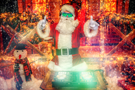 DJ Santa Claus in luminous glasses and headphones holds a party near his house decorated with lights. Christmas songs and music.の写真素材