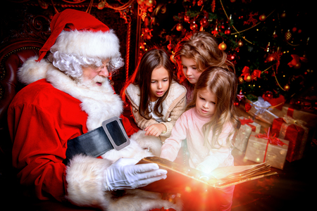 Happy young girls are sitting with Santa Claus at home. Merry Christmas and Happy New Year. Miracle time.の写真素材