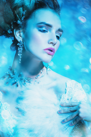 A close up portrait of a cold beautiful lady with a fan posing in the studio over the blue background. Beauty,cosmetics, hairstyle.の写真素材