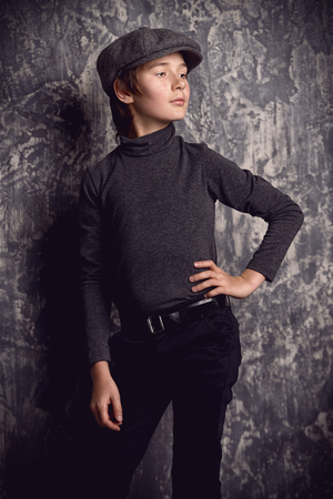 Kid's fashion. Modern boy is posing in dark clothes and hat at studio. Clothes for children.の写真素材