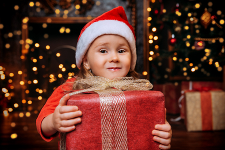 A portrait of a happy cute girl holding a gift box at home with festive decorations. Merry Christmas and Happy New Year. Time for miracles.の写真素材