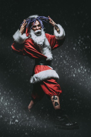 Full length portrait of a cool punk Santa Claus with bright dreadlocks over black background.の写真素材