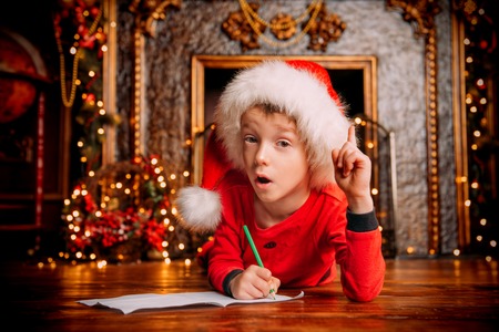 A portrait of a young boy writing a letter with wishes to Santa Claus. Decorations for Christmas and New Year. Time for miracles.の写真素材