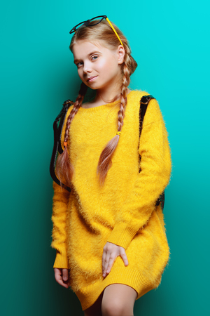 Cute nine year old girl posing in studio in fluffy yellow dress over blue background. Children's beauty and fashion.の写真素材