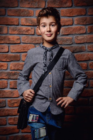 Kid's fashion. Modern nine year old boy posing at studio over brick wall background. Clothes and accessories for children.の写真素材