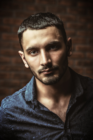 Close-up portrait of a handsome brunet man over brick wall background. Men's beauty, fashion. Men's barbershop, Hairstyle.の写真素材