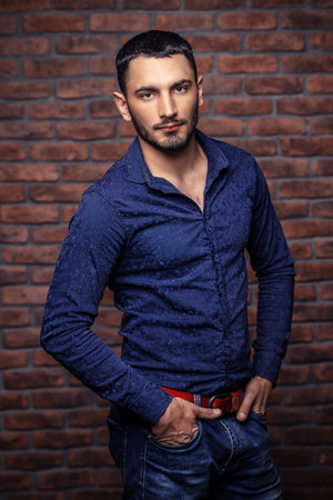Portrait of a handsome brunet man standing by a brick wall. Men's beauty, fashion. Men's barbershop,...