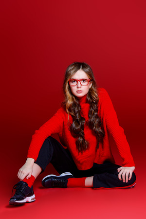 Teen style. Beautiful female model with long hair posing at studio in youth clothes. Red background. Beauty, fashion.の写真素材