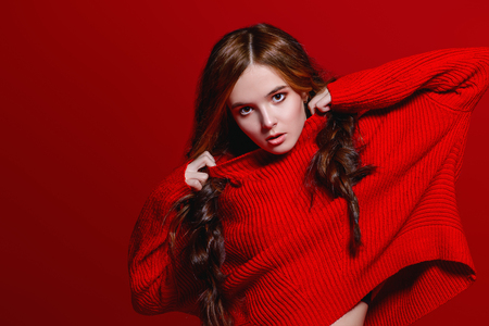 Teen style. Beautiful female model with long hair posing at studio in youth clothes. Red background. Beauty, fashion.の写真素材