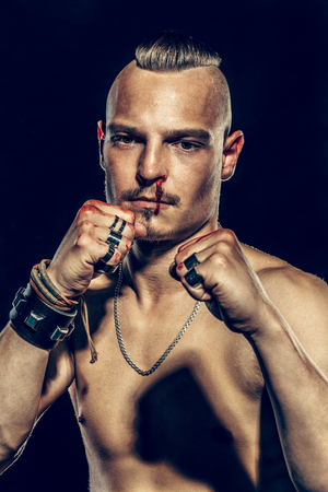 Fight club, MMA. Portrait of a bad guy fighter with a face in the blood, demonstrating his muscles and strength. Rocker, punk.の写真素材