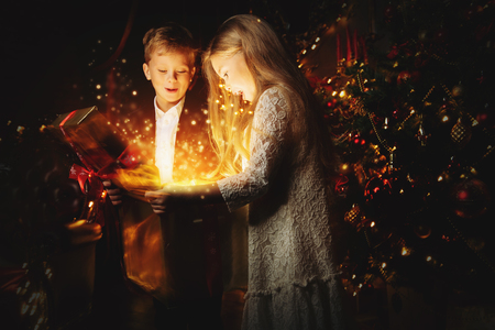 A portrait of children opening a gift box. Merry Christmas, happy New Year. Luxurious apartment with christmas lights and decorations. Miracle time.の写真素材