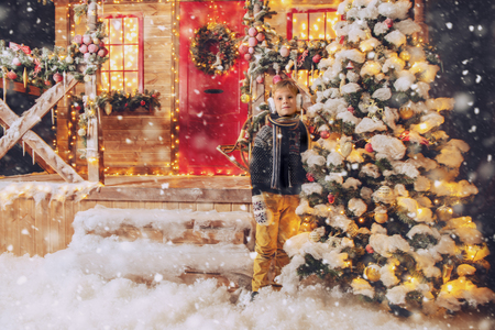 A portrait of a boy near the Christmas tree outdoor. Merry Christmas, happy New Year. Yard with a christmas tree, lights and decorations. Miracle time.の写真素材