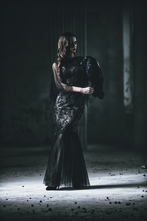 A beautiful brunette lady with a raven in ruins. Evening dress. Fashion, beauty.の写真素材