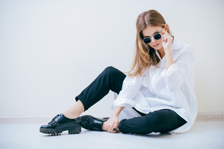 Portrait of a cute girl teenager with sunglasses sitting on the floor in the room. Glasses for a modern young generation. Beauty, fashion.の写真素材