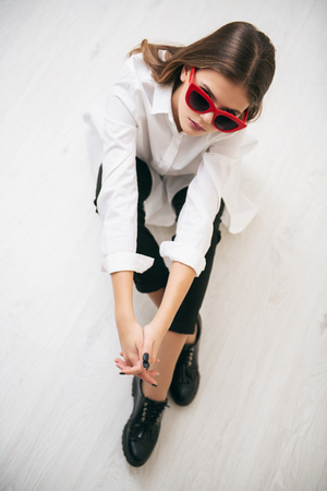 Portrait of a cute girl teenager with sunglasses sitting on the floor in the room. Glasses for a modern young generation. Beauty, fashion.の写真素材