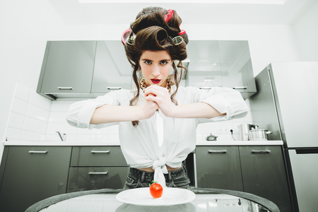 An attractive girl in everyday clothes and curlers is tasting a dish in the kitchen. Cooking in the kitchen. Gastronomic concept.の写真素材