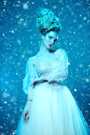 A portrait of a cold beautiful lady wearing a fluffy dress and posing on a snowy blue background. Beauty,cosmetics, hairstyle, fashion.の写真素材
