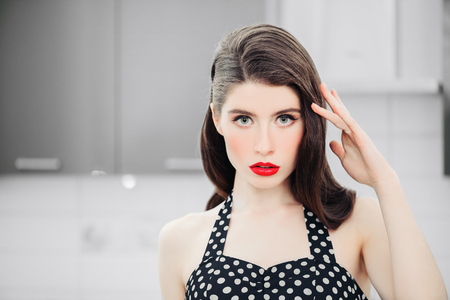 Portrait of attractive young woman in a black dress with white dots  is posing on kitchen background. Pin-up style.の写真素材