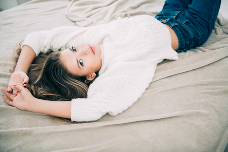 Portrait of a cute girl teenager lying on the bed in the bedroom. Beauty, fashion.の写真素材