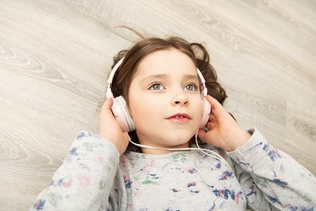 A pretty little girl is lying with headphones on the floor. Fashion home shot. Childhood. Kid's fashion.の写真素材