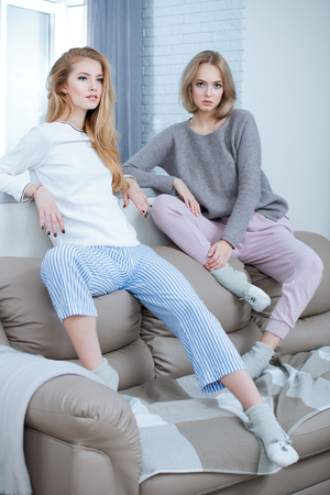 Two girlfriends are posing  in home clothes in interior. Beauty, fashion.の写真素材