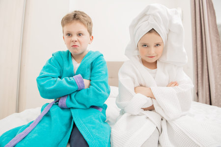 Cute girl and boy lie in bathrobes in bed at home. Fashion home shot. Childhood. Kid's fashion.の写真素材