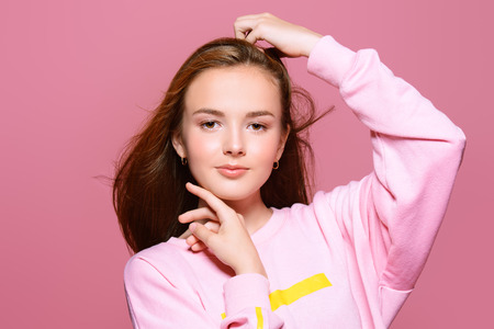 Teen style. Beautiful young model with long hair posing at studio in jeans and pink sweatshirt. Beauty, fashion.の写真素材