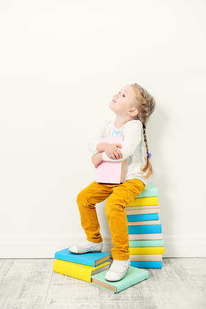 A portrait of a cute pretty girl sitting on the textbooks over the white background. Beauty, fashion, school, education.の写真素材