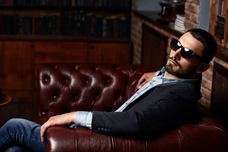 Portrait of a sexy handsome man on a leather sofa. Fashion shot. Men's beauty, fashion. Men's barbershop, Hairstyle.の写真素材