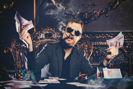 A wealthy mature man smoking cigar and playing poker in a casino. Gambling, playing cards and roulette.の写真素材
